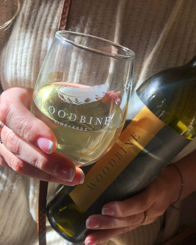 Holding glass of Woodbine Vineyard's white wine and bottle